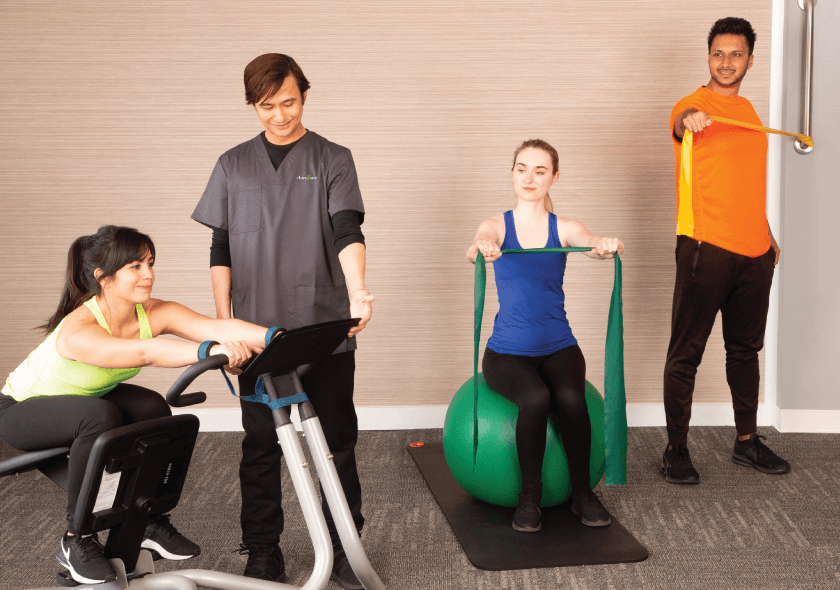 A chiropractic technician helps three patients perform active rehabilitative therapies using the Precor stretcher and resistance bands.